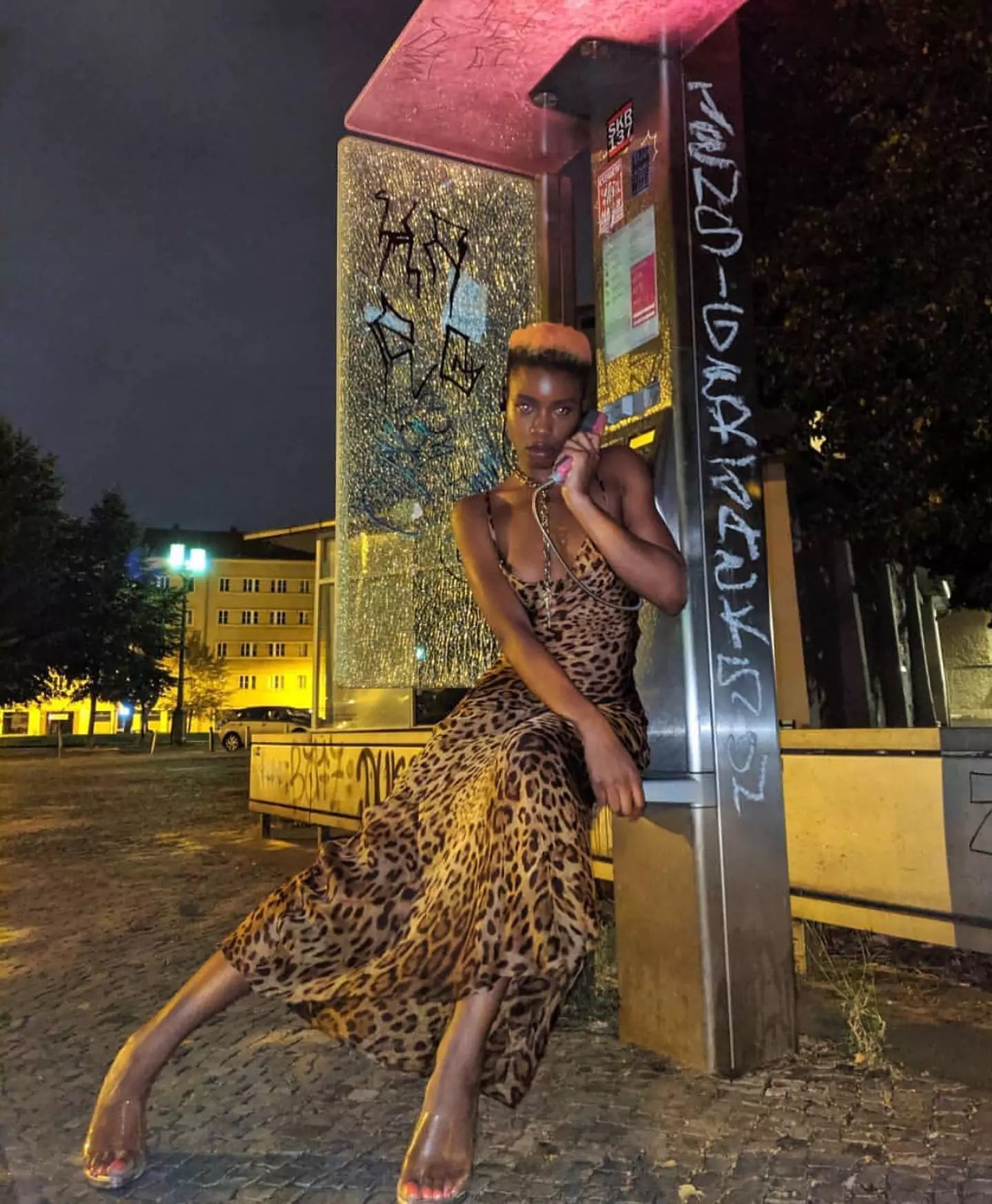 A woman in a leopard print dress posing in front of a phone booth.