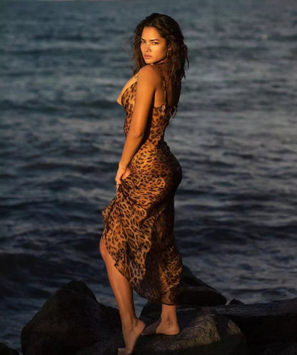 A woman in a leopard print dress standing on rocks by the ocean.
