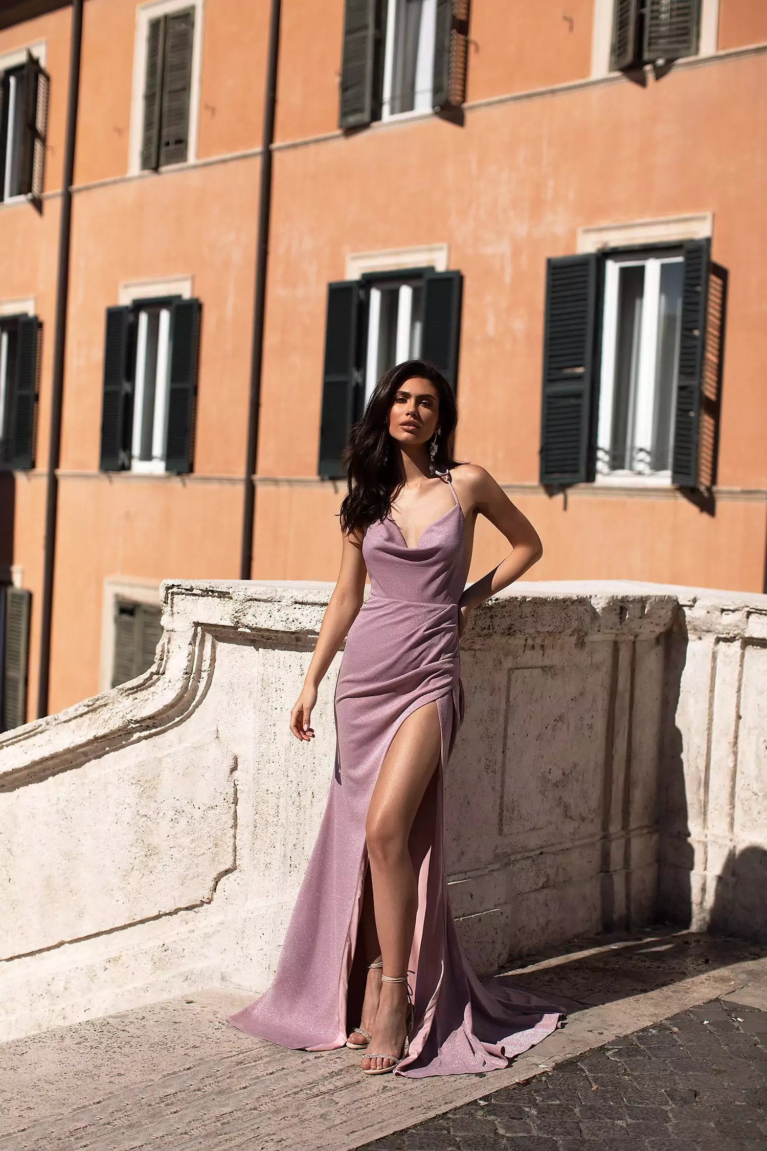 A woman in a purple Sena lilac gown leaning against a wall