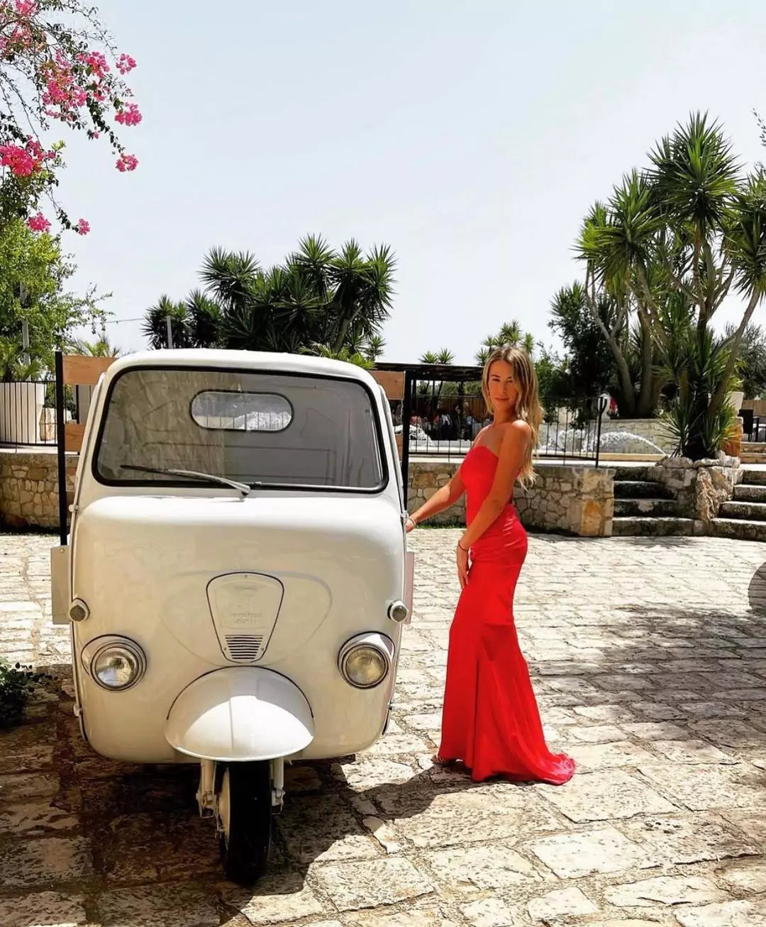 A woman in a red dress standing next to a white car.