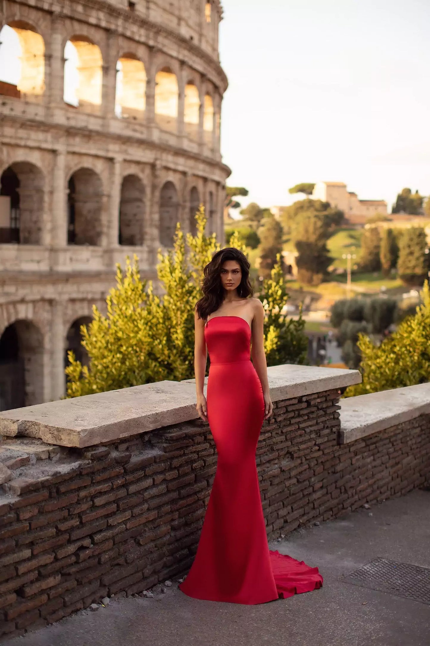 A woman in a red gown is posing in front of the colosseum