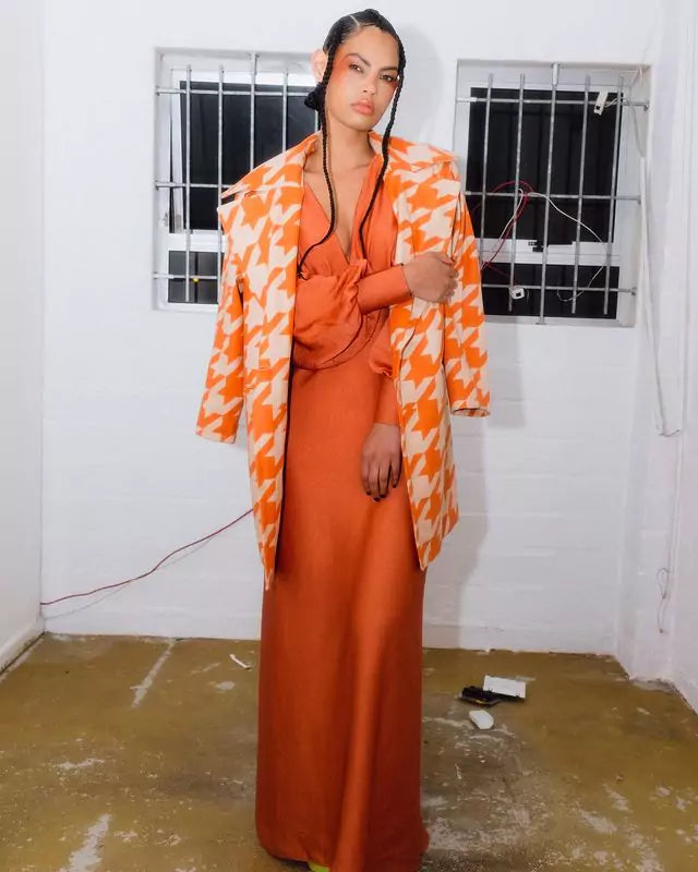 A woman in an orange dress posing in a white room.