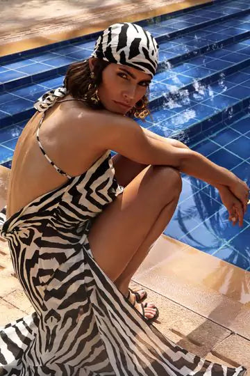 A woman in Zagora Monochrome Semi Sheer Dress sitting on the edge of a swimming pool
