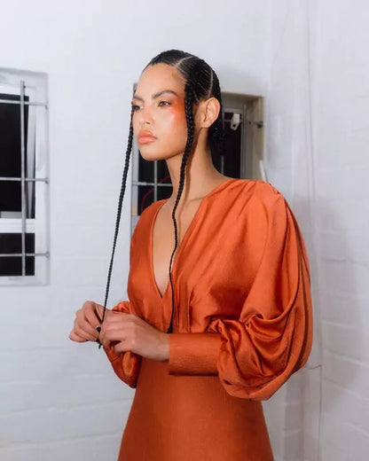A model in an orange dress is posing in front of a mirror.
