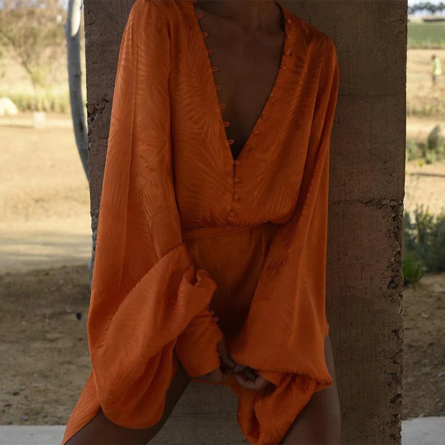 A woman in an orange romper leaning against a wall.