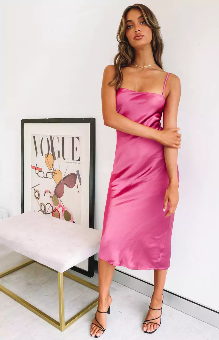 A woman in a pink slip dress posing in front of a white wall.