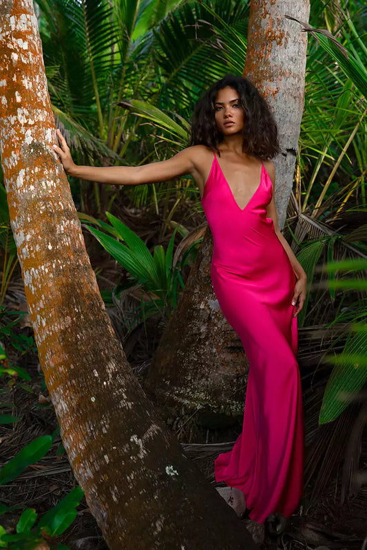 A woman in a pink dress leaning against a tree.