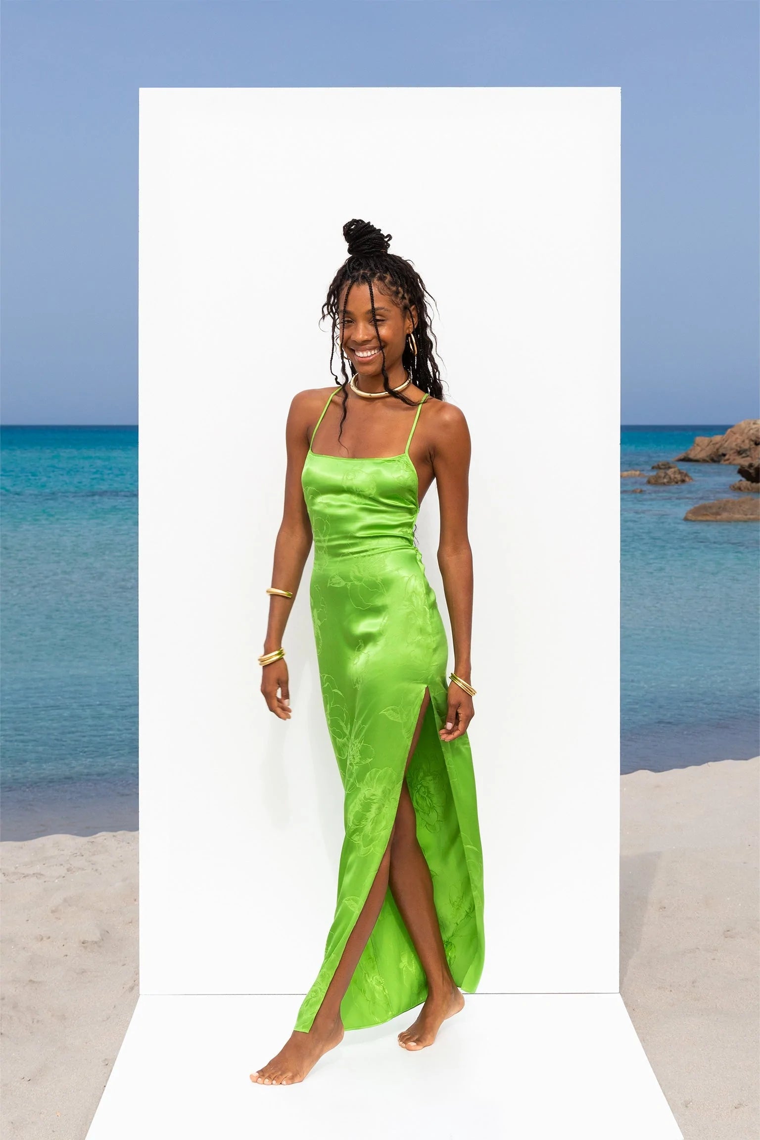 A woman in a lime green dress posing on the beach.