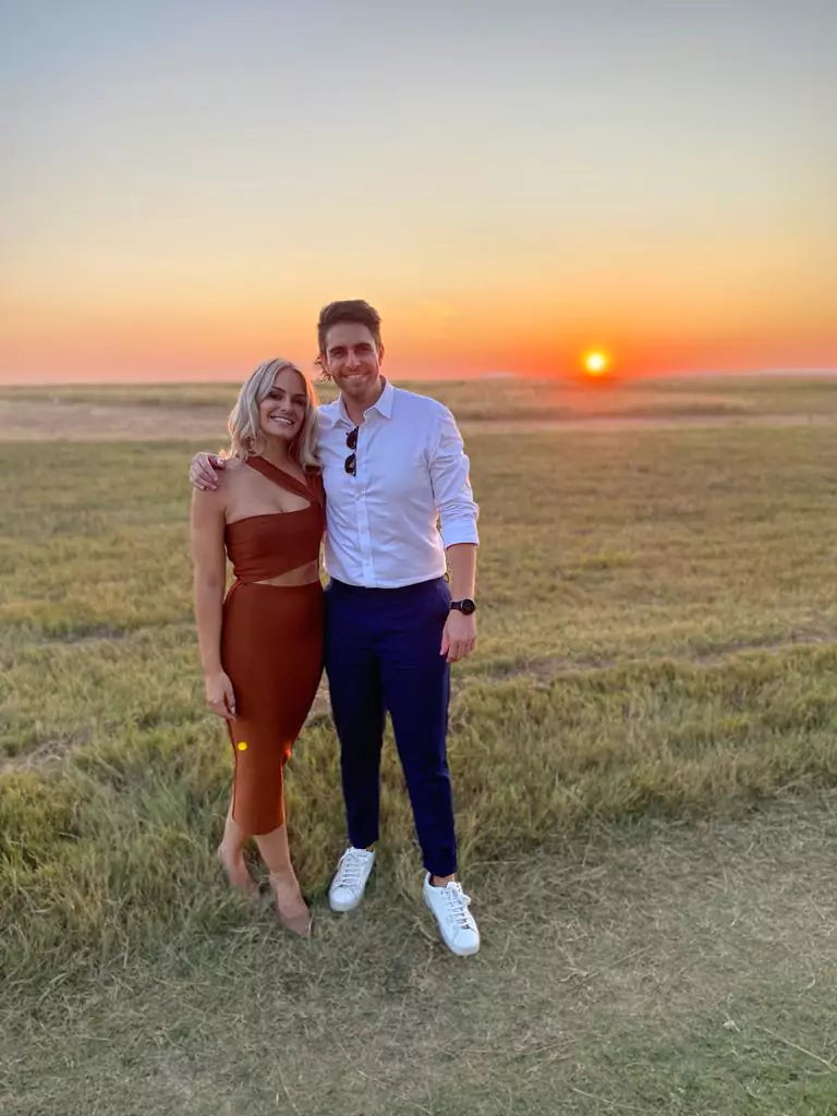 A man and woman standing in a field at sunset.