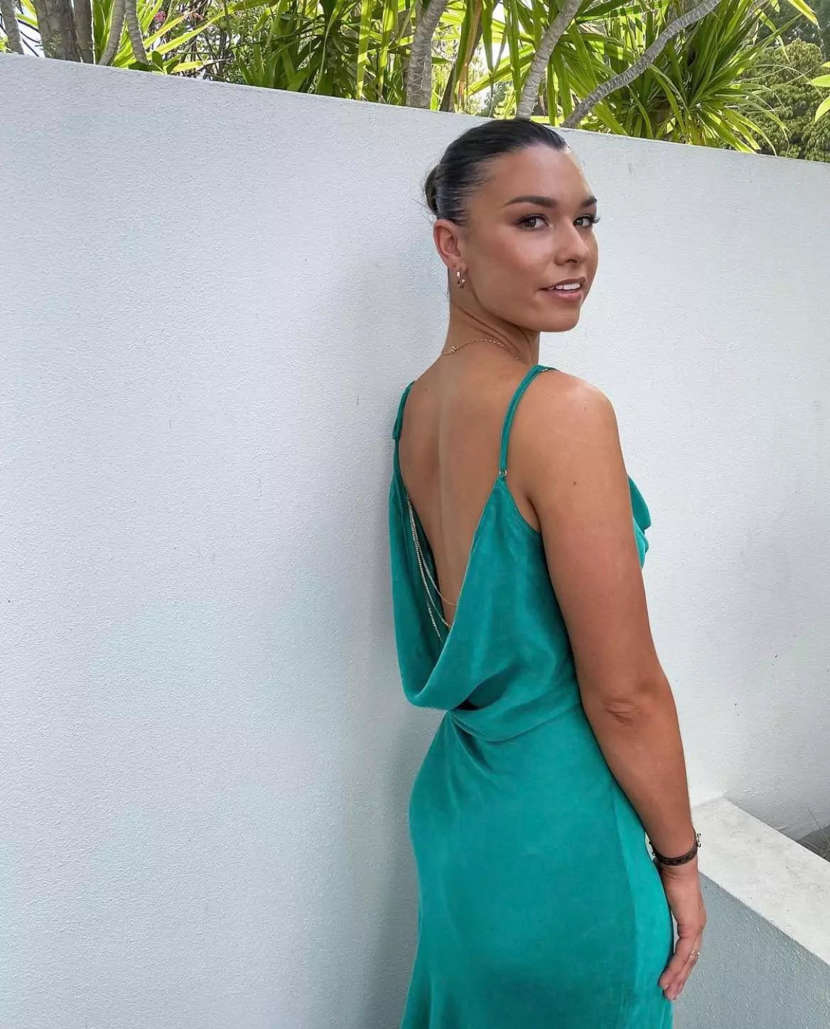 A woman in a green dress posing against a wall.