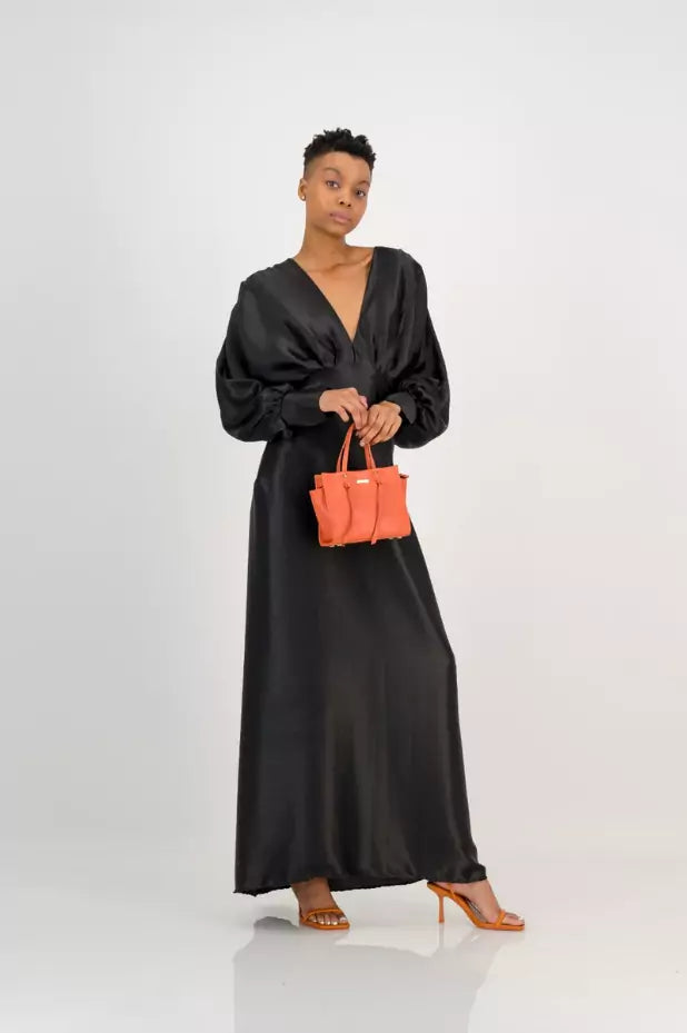 The model is wearing a black maxi dress with an orange handbag.