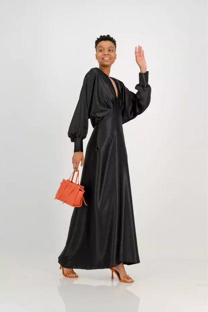 A woman wearing a black maxi dress and orange handbag.