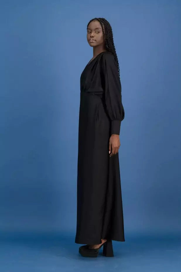 A woman wearing a black maxi dress standing on a blue background.