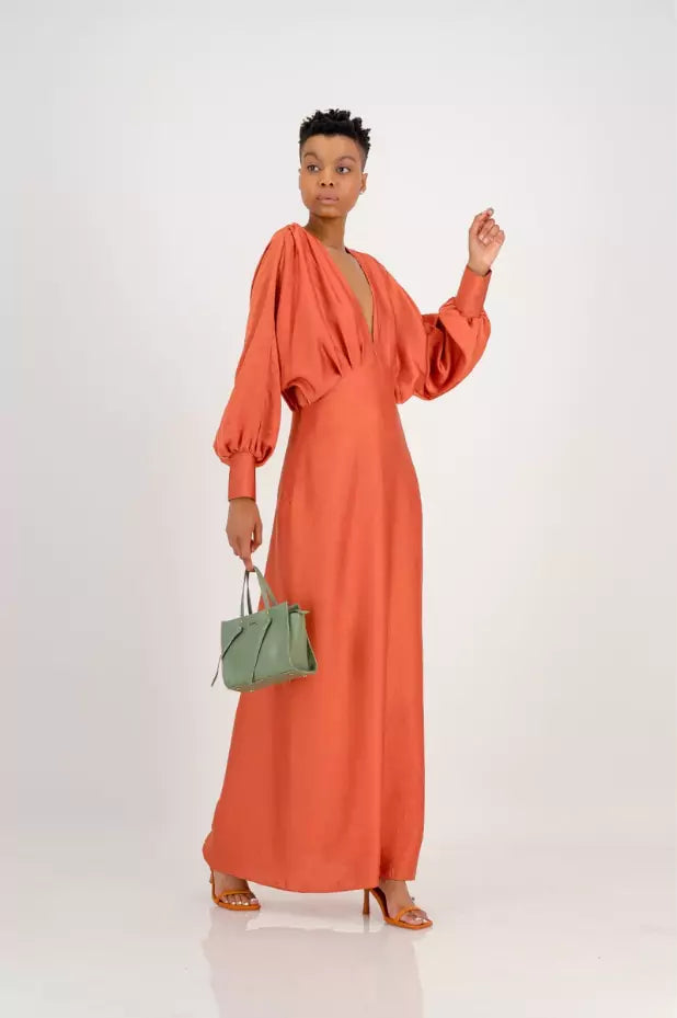 The model is wearing a Samiya Rust Satin Maxi Dress with a green purse, creating the perfect evening look.