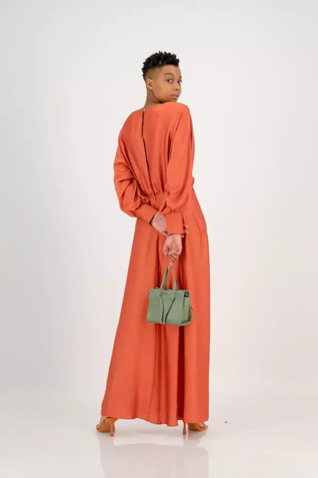 The back view of a woman wearing an orange maxi dress with a green handbag.
