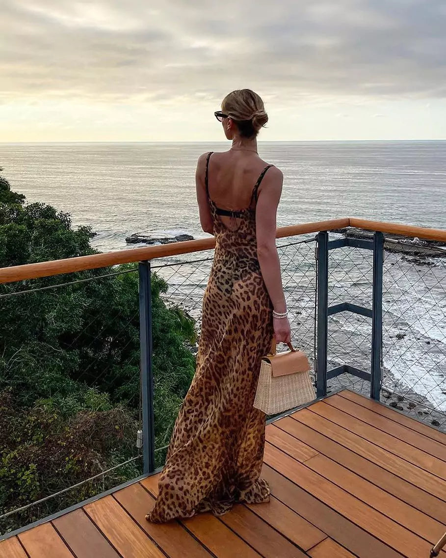 A woman in a leopard print dress standing on a deck overlooking the ocean.