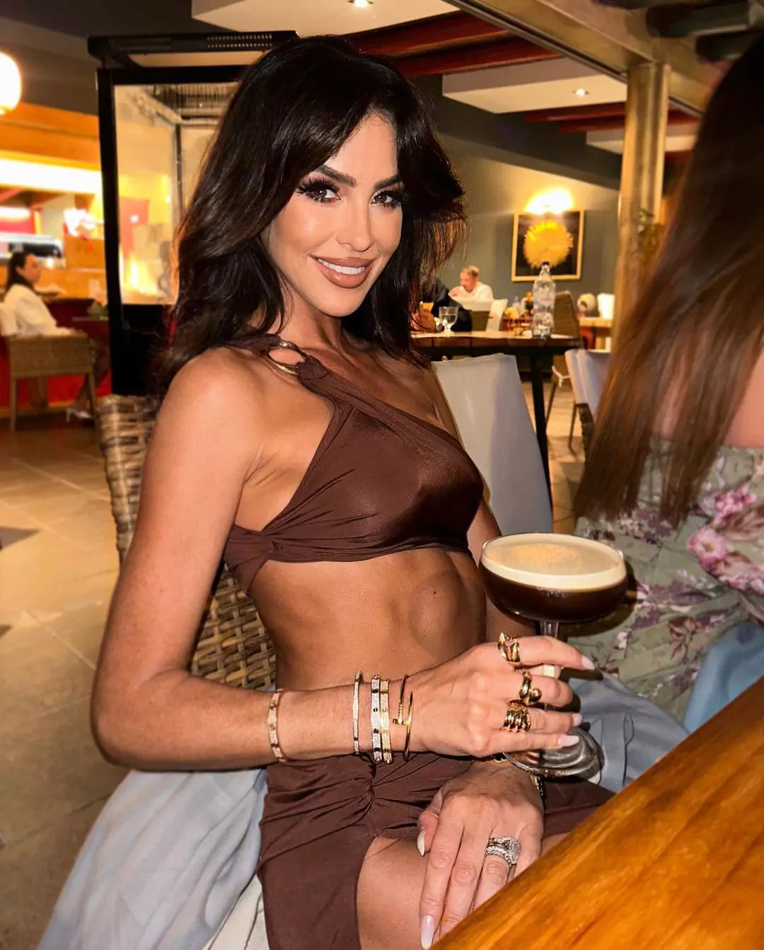 A woman wearing the Caterina Cocoa Cut Out Maxi Dress, sitting at a table with a drink.