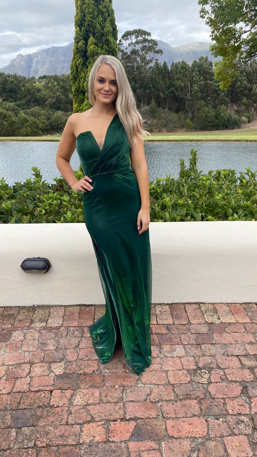 A woman in a green dress poses in front of a lake.