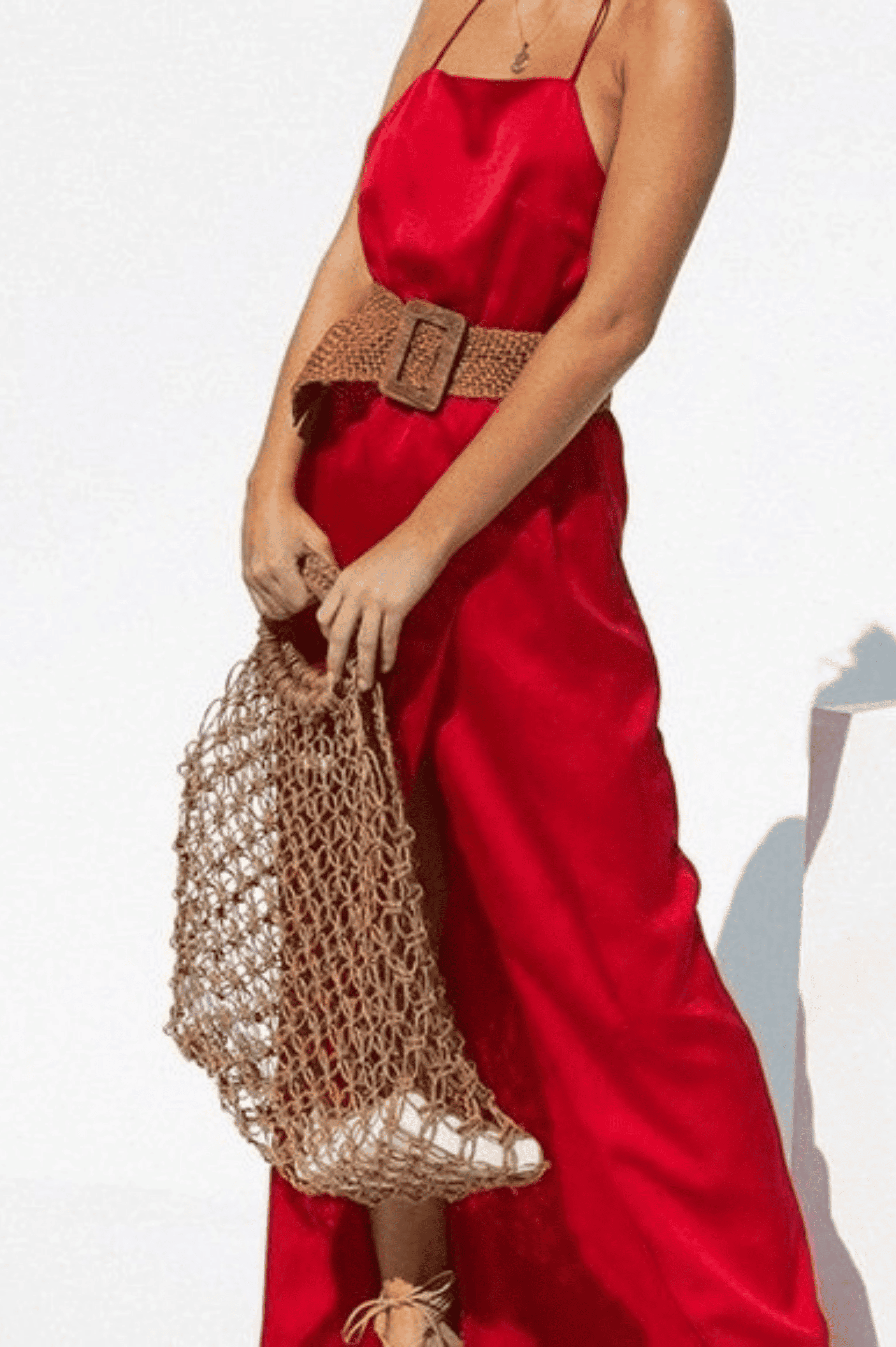A woman in a red maxi dress holding a rattan bag.