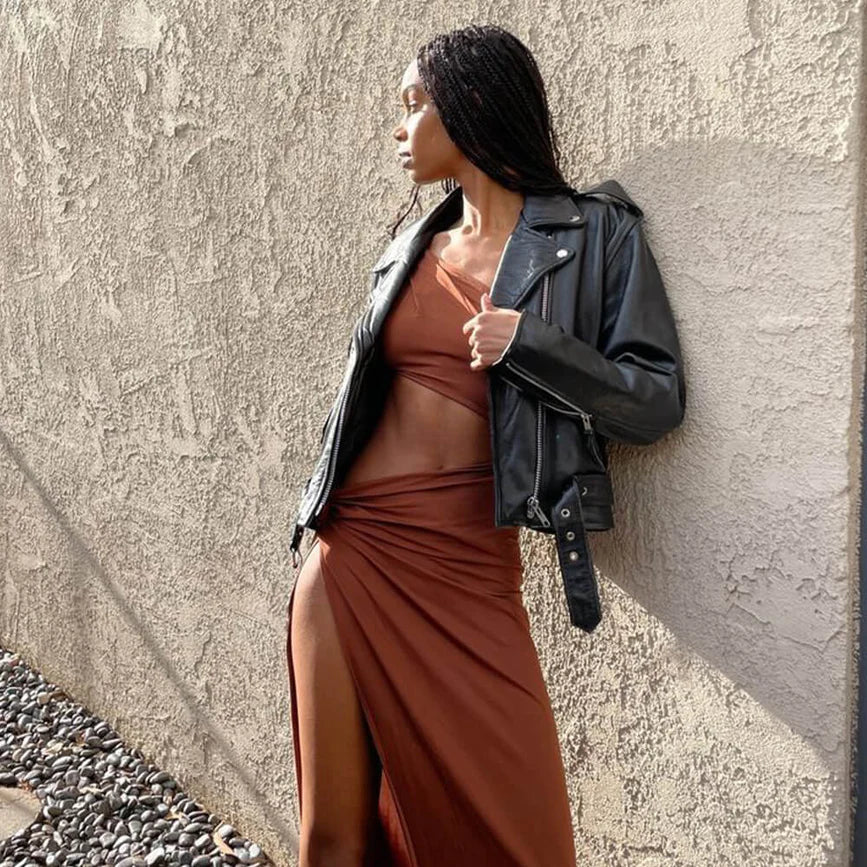 A woman in a brown dress, called Caterina Cocoa Cut Out Maxi Dress, leaning against a wall.