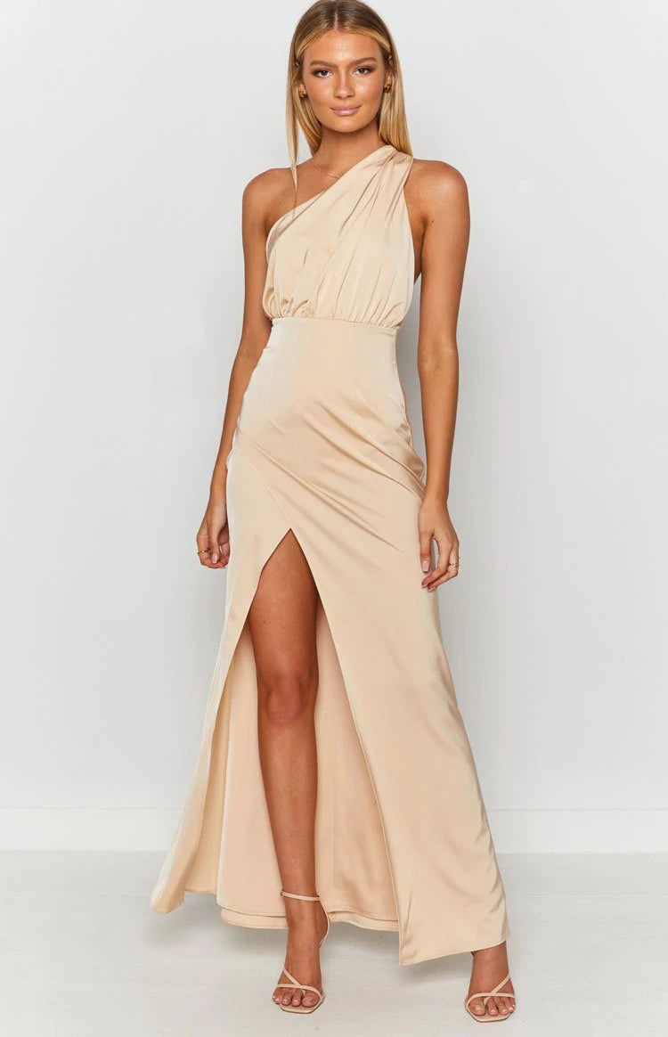 The model is wearing a nude maxi dress with a slit.