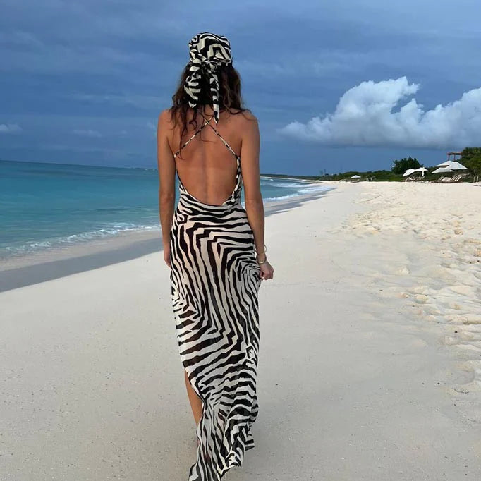 A woman in a zebra print dress walking on the beach.