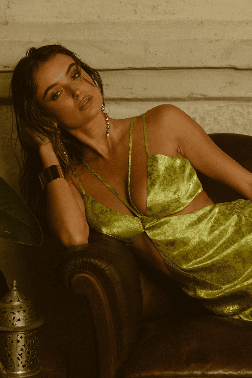 A woman in a green dress laying on a leather chair.